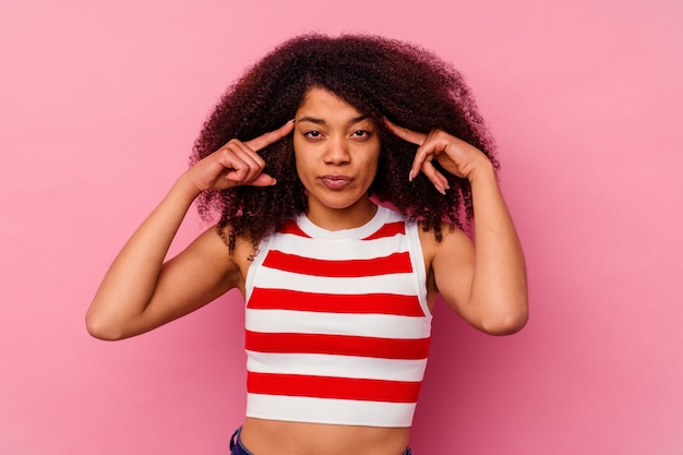 Photo young african american woman isolated on pink focused on a task, keeping forefingers pointing head.