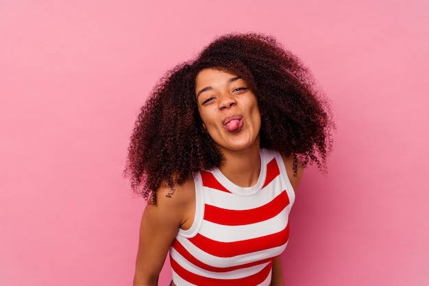 Giovane donna afroamericana isolata su rosa divertente e amichevole che attacca fuori la lingua.