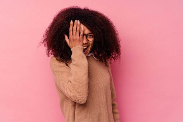 Young african american woman isolated on pink having fun covering half of face with palm.