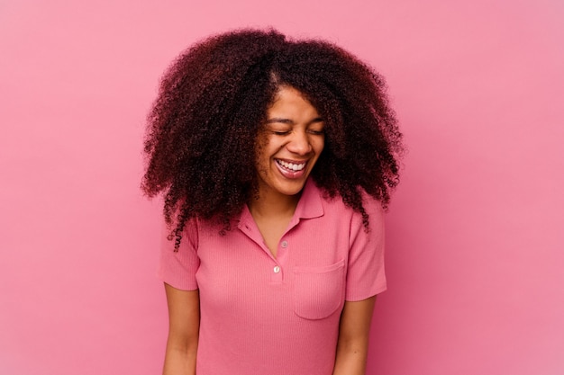 Young african american woman isolated on pink laughs and closes eyes, feels relaxed and happy.