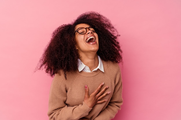 Young african american woman isolated on pink laughs happily and has fun keeping hands on stomach.