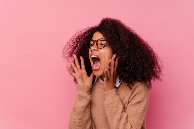 Young african american woman isolated on pink shouts loud, keeps eyes opened and hands tense.