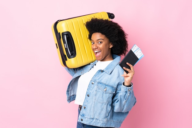 Young African American woman isolated on pink in vacation with suitcase and passport