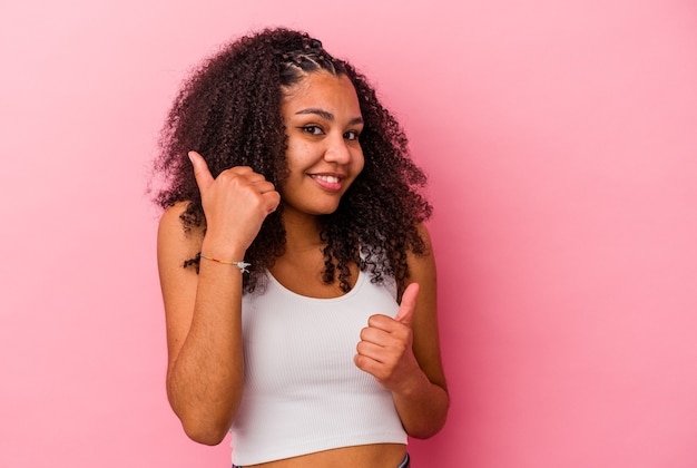 Young african american woman isolated on pink wall raising both thumbs up, smiling and confident.