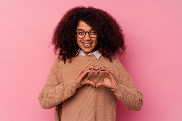 Young african american woman isolated on pink wall smiling and showing a heart shape with hands.