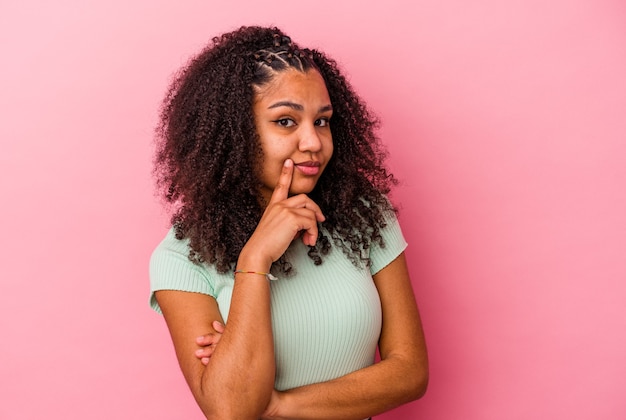 ピンクの壁に孤立した若いアフリカ系アメリカ人女性は、皮肉な表情で不幸に見えます。