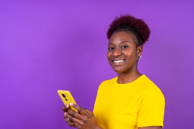 Young african american woman isolated on a purple background smiling with the mobile phone study session