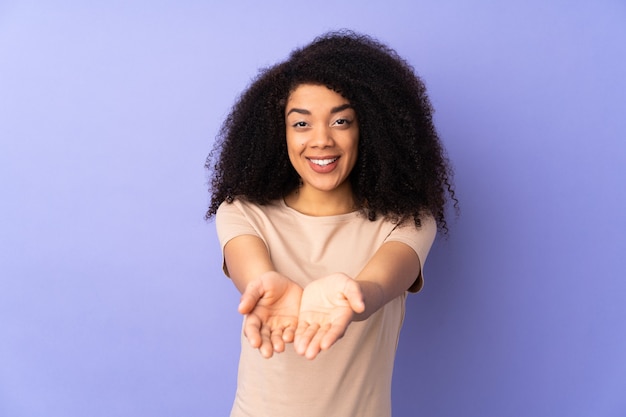 Young african american woman isolated on purple holding copyspace imaginary on the palm to insert an ad