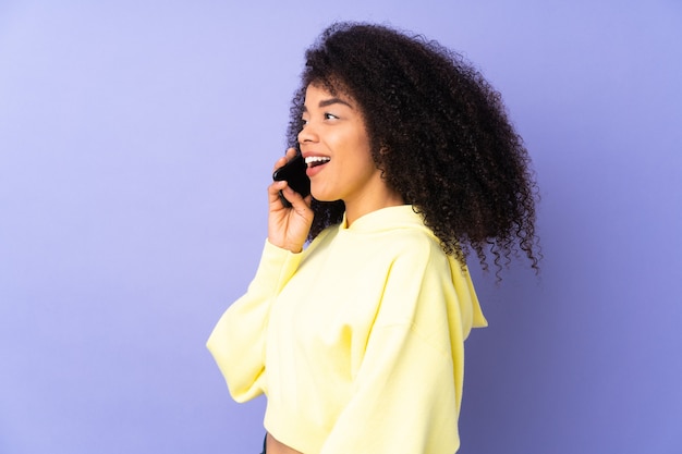 Giovane donna afroamericana isolata su viola mantenendo una conversazione con il telefono cellulare