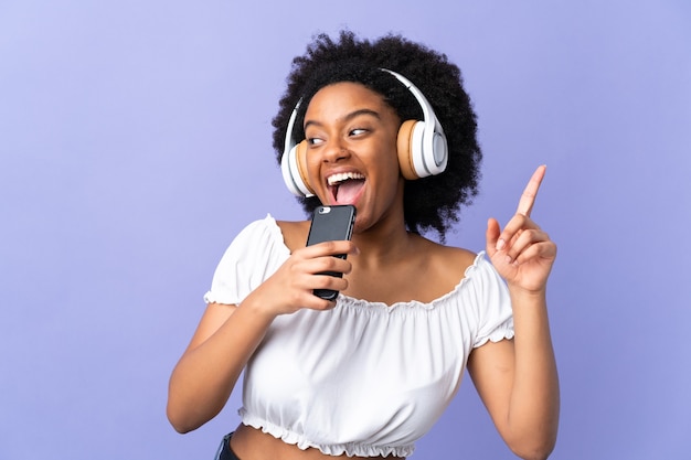 Young African American woman isolated on purple listening music with a mobile and singing