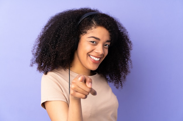 Young african american woman isolated on purple wall listening music