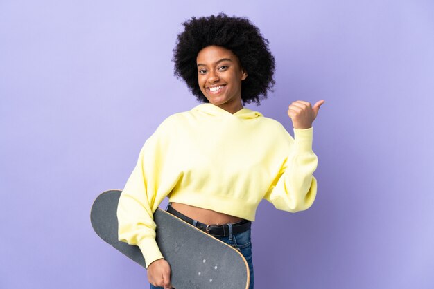 Young African American woman isolated on purple wall with a skate and pointing to the side