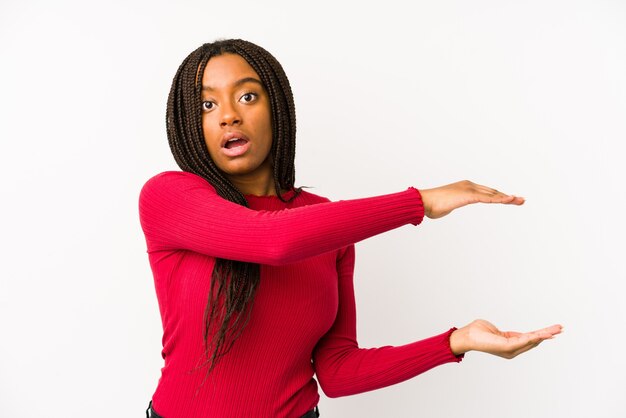 Young african american woman isolated shocked and amazed holding a copy space between hands.