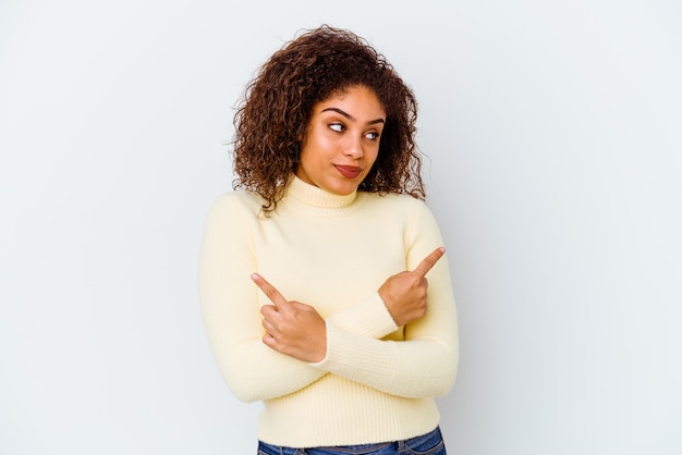 Photo young african american woman isolated on white background points sideways, is trying to choose between two options.