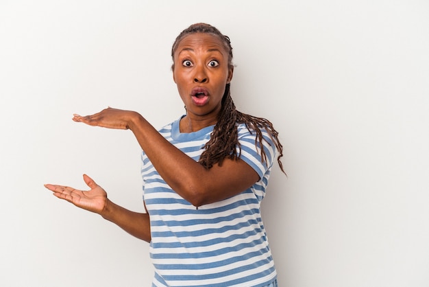 Young african american woman isolated on white background shocked and amazed holding a copy space between hands.