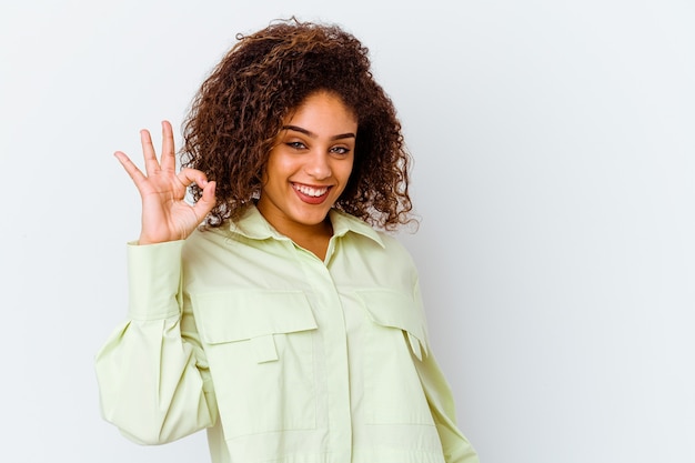 Foto la giovane donna afroamericana isolata su fondo bianco strizza l'occhio e tiene un gesto giusto con la mano.