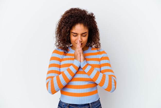 Young african american woman isolated on white wall holding hands in pray near mouth, feels confident.