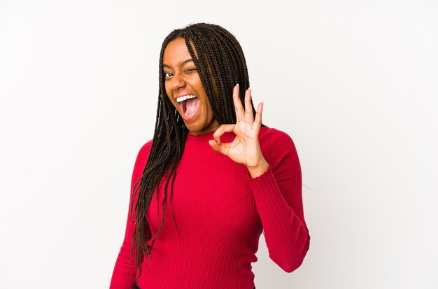 Young african american woman isolated winks an eye and holds an okay gesture with hand.