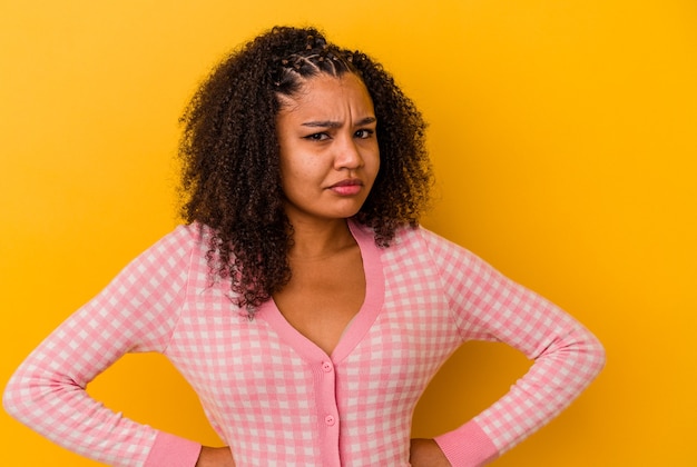 Young african american woman isolated on yellow background blows cheeks, has tired expression. Facial expression concept.