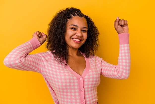 Young african american woman isolated on yellow background celebrating a special day, jumps and raise arms with energy.