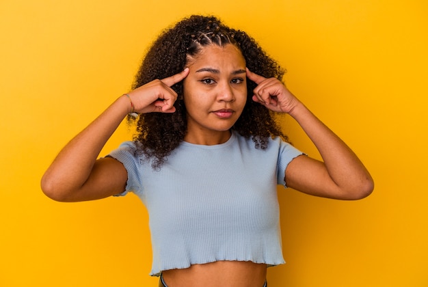 Young african american woman isolated on yellow background focused on a task, keeping forefingers pointing head.