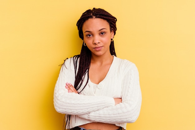 Foto la giovane donna afroamericana isolata sul fronte accigliato sfondo giallo con dispiacere, tiene le braccia conserte.