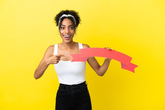Young african american woman isolated on yellow background holding an empty placard with surprised expression