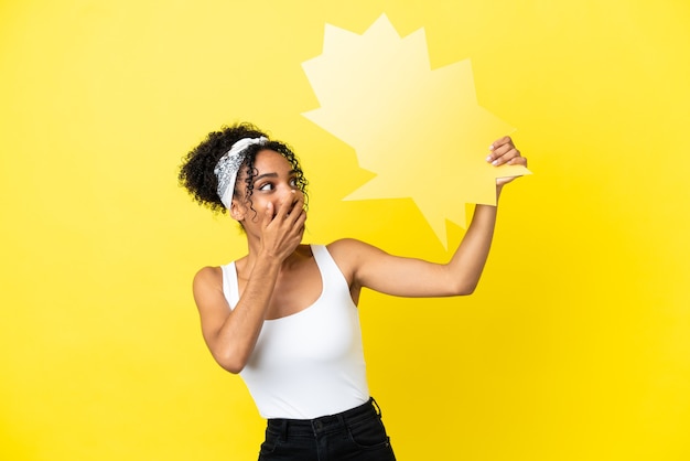 Young african american woman isolated on yellow background holding an empty speech bubble with surprised expression