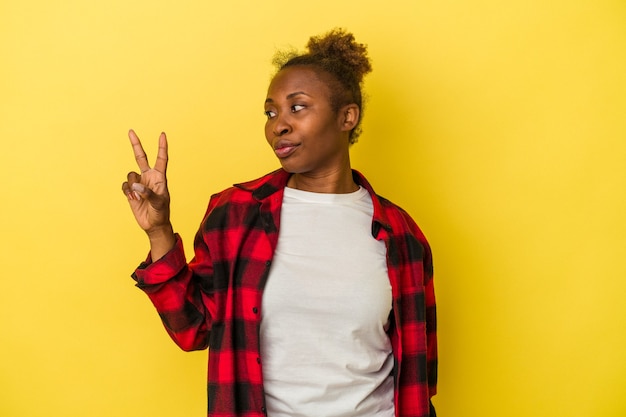 Young african american woman isolated on yellow background joyful and carefree showing a peace symbol with fingers.