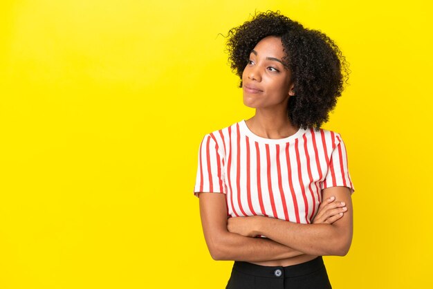 Young african american woman isolated on yellow background looking to the side