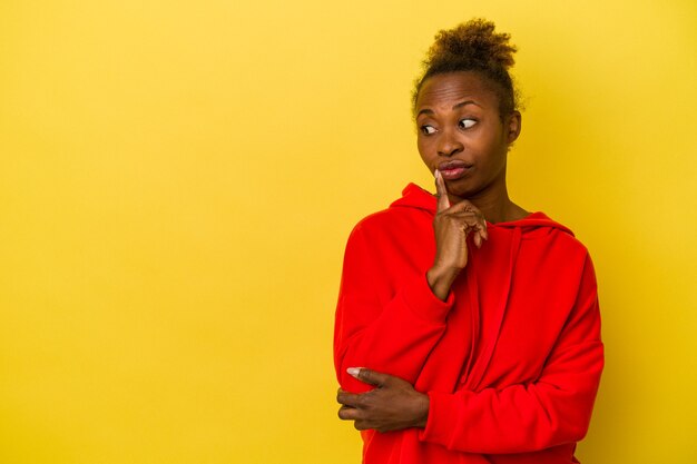 Young african american woman isolated on yellow background looking sideways with doubtful and skeptical expression.