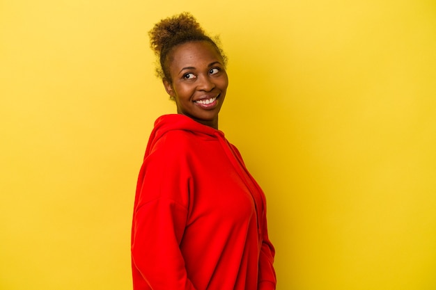 Foto la giovane donna afroamericana isolata su fondo giallo guarda da parte sorridente, allegra e piacevole.