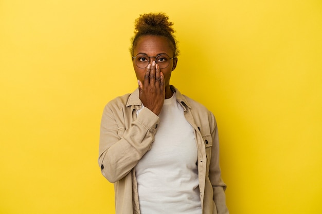 Young african american woman isolated on yellow background shocked, covering mouth with hands, anxious to discover something new.