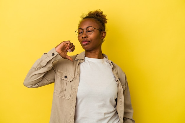 Giovane donna afroamericana isolata su sfondo giallo che mostra un gesto di antipatia, pollice in giù. concetto di disaccordo.