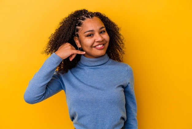 Young african american woman isolated on yellow background showing a mobile phone call gesture with fingers.