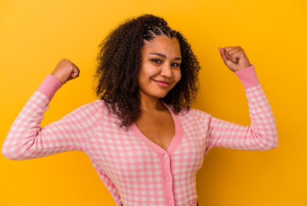 Young african american woman isolated on yellow background showing strength gesture with arms, symbol of feminine power