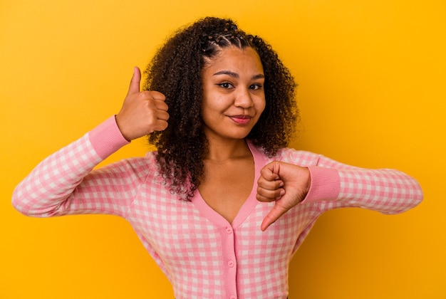 Young african american woman isolated on yellow background showing thumbs up and thumbs down, difficult choose concept