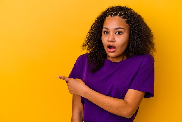 Young african american woman isolated on yellow background smiling and pointing aside, showing something at blank space.