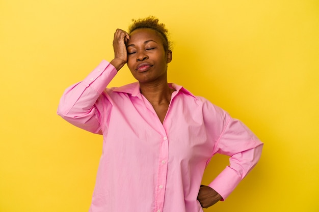 Young african american woman isolated on yellow background tired and very sleepy keeping hand on head.