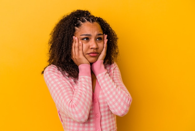 黄色の背景に分離された若いアフリカ系アメリカ人女性は、泣き言を言い、悲しげに泣いています。