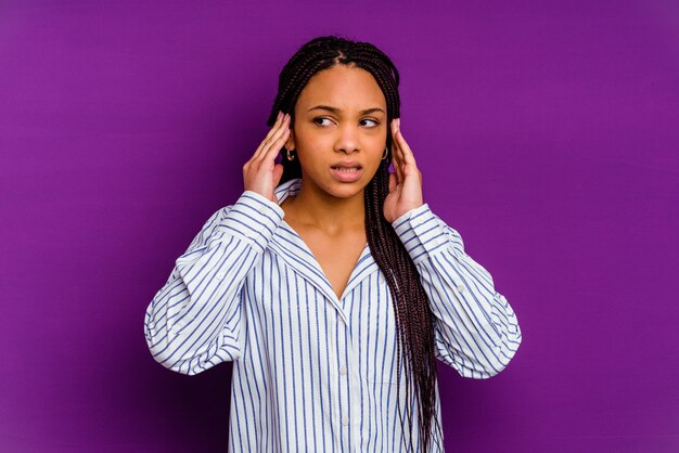 Giovane donna afro-americana isolata su giallo che copre le orecchie con le dita, stressata e disperata da un ambiente rumoroso.