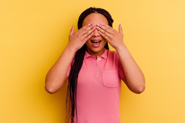 黄色で隔離された若いアフリカ系アメリカ人の女性は手で目を覆い、驚きを広く待っている笑顔。