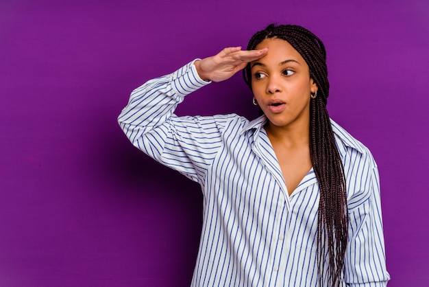 Young african american woman isolated on yellow  looking far away keeping hand on forehead.