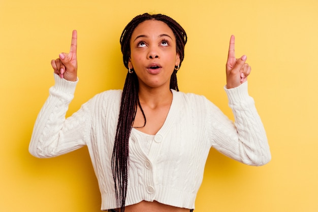 Young african american woman isolated on yellow pointing upside with opened mouth.