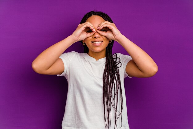 Young african american woman isolated on yellow showing okay sign over eyes