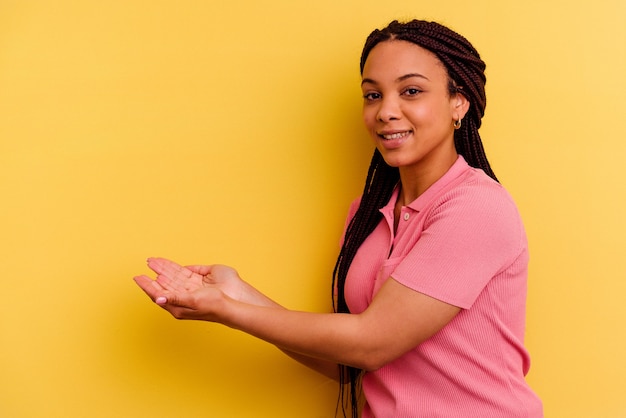 Foto giovane donna afroamericana isolata sulla parete gialla che tiene uno spazio della copia su una palma.