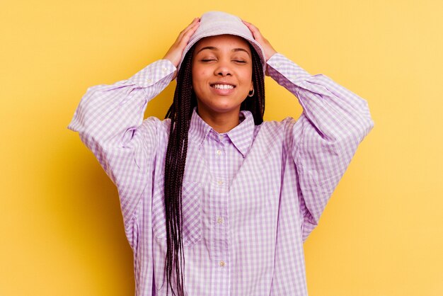 Young african american woman isolated on yellow wall laughs joyfully keeping hands on head. Happiness concept.