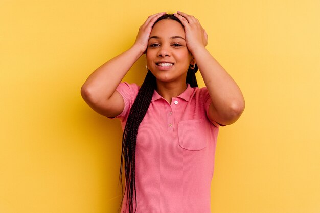 Young african american woman isolated on yellow wall laughs joyfully keeping hands on head