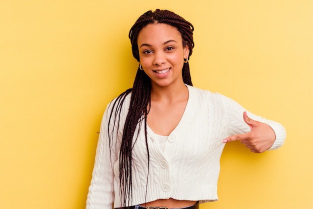 Foto giovane donna afroamericana isolata sulla persona del muro giallo che indica a mano uno spazio della copia della camicia, orgoglioso e fiducioso