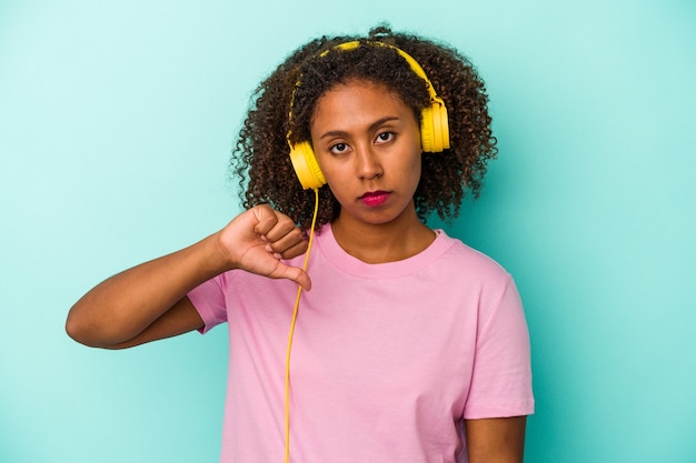 Young african american woman listening to music isolated on blue background showing a dislike gesture, thumbs down. Disagreement concept.